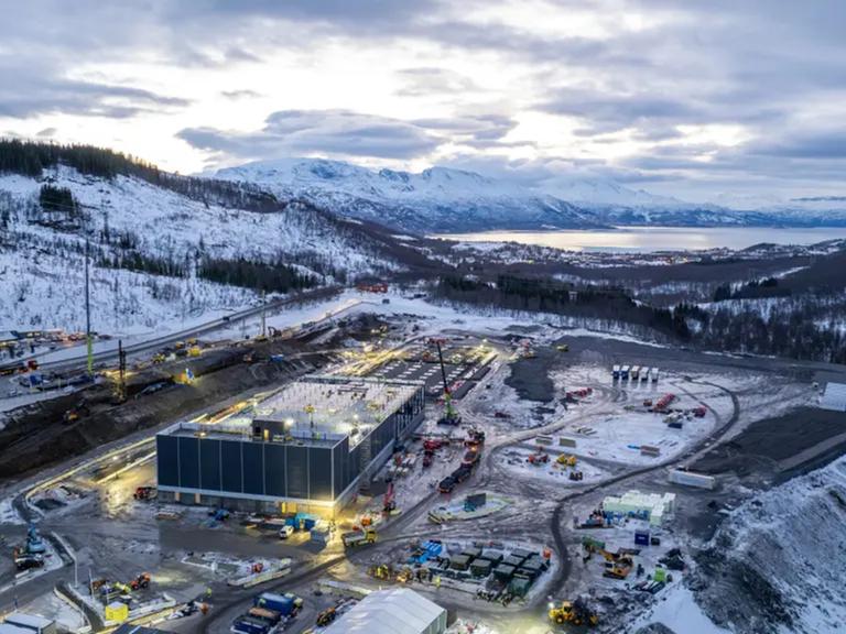 Eine Drohnenaufnahme des neu gebauten KI-Rechenzentrums in Narvik, Norwegen bei Dämmerung. Im Hintergrund schneebedeckte Berge und ein Fjord