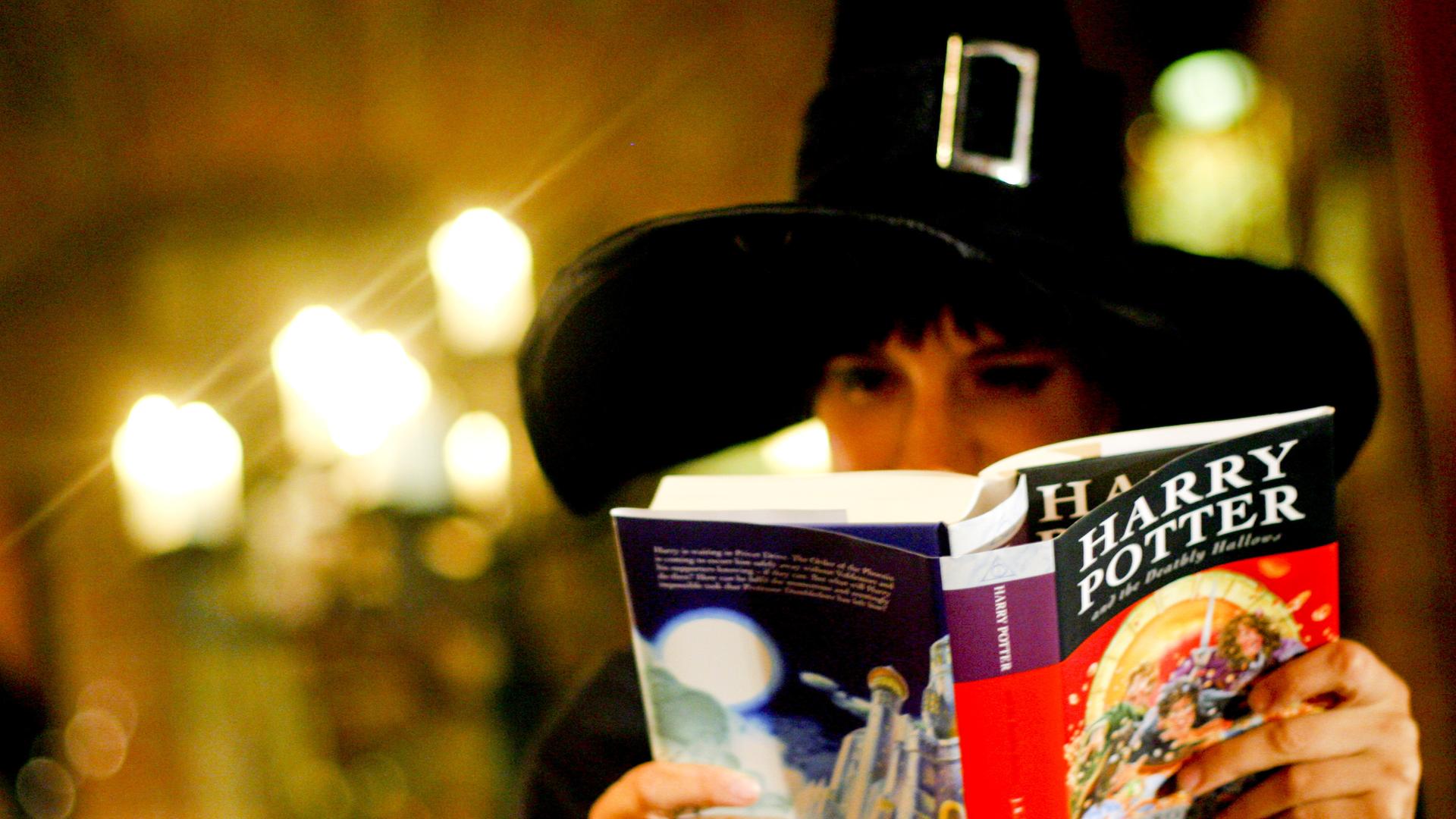 Jemand trägt einen Zauber-Hut und liest ein Harry-Potter-Buch.