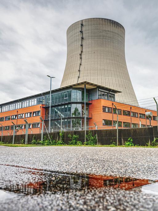 Der Kühlturm des stillgelegte Kernkraftwerks Isar 2. Davor ein orangefarbenes Gebäude.