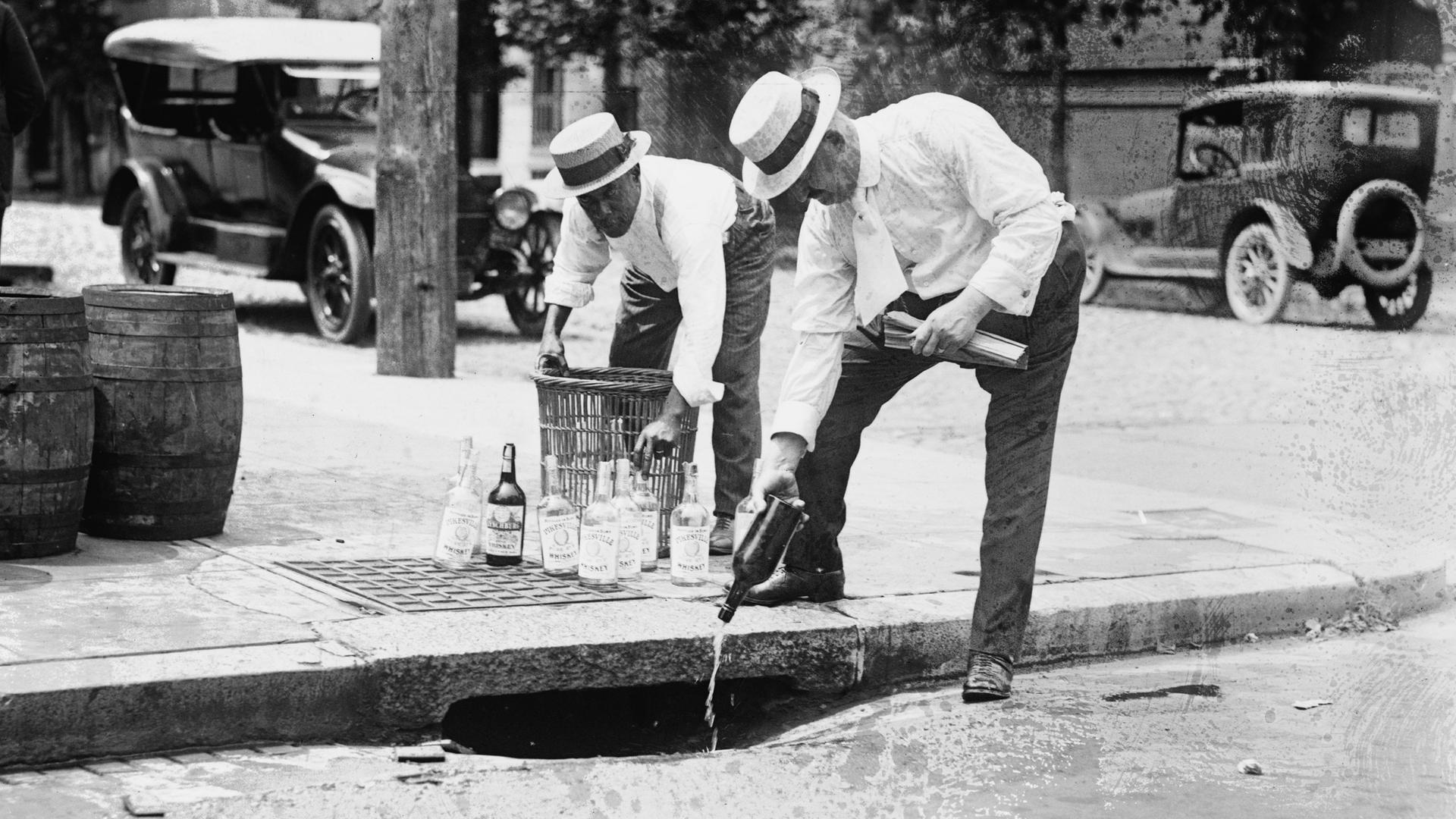 Männer schütten Alkohol in einen Abwasserkanal auf der Straße