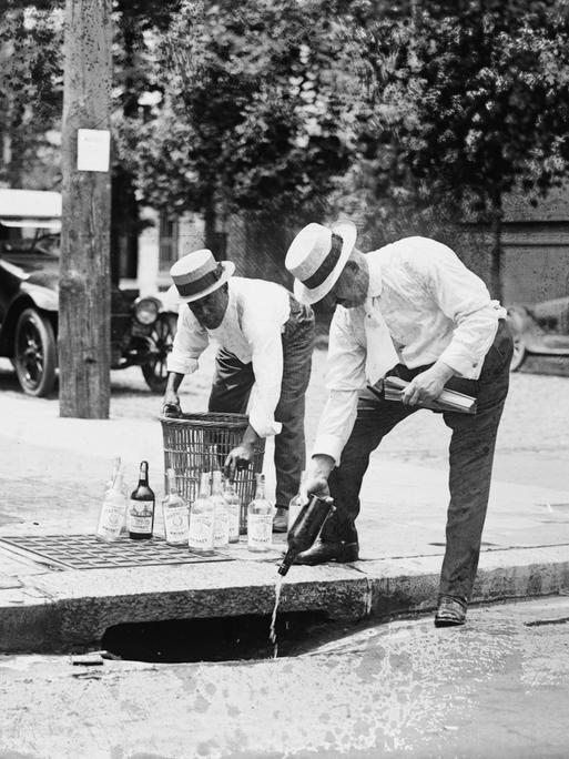 Männer schütten Alkohol in einen Abwasserkanal auf der Straße