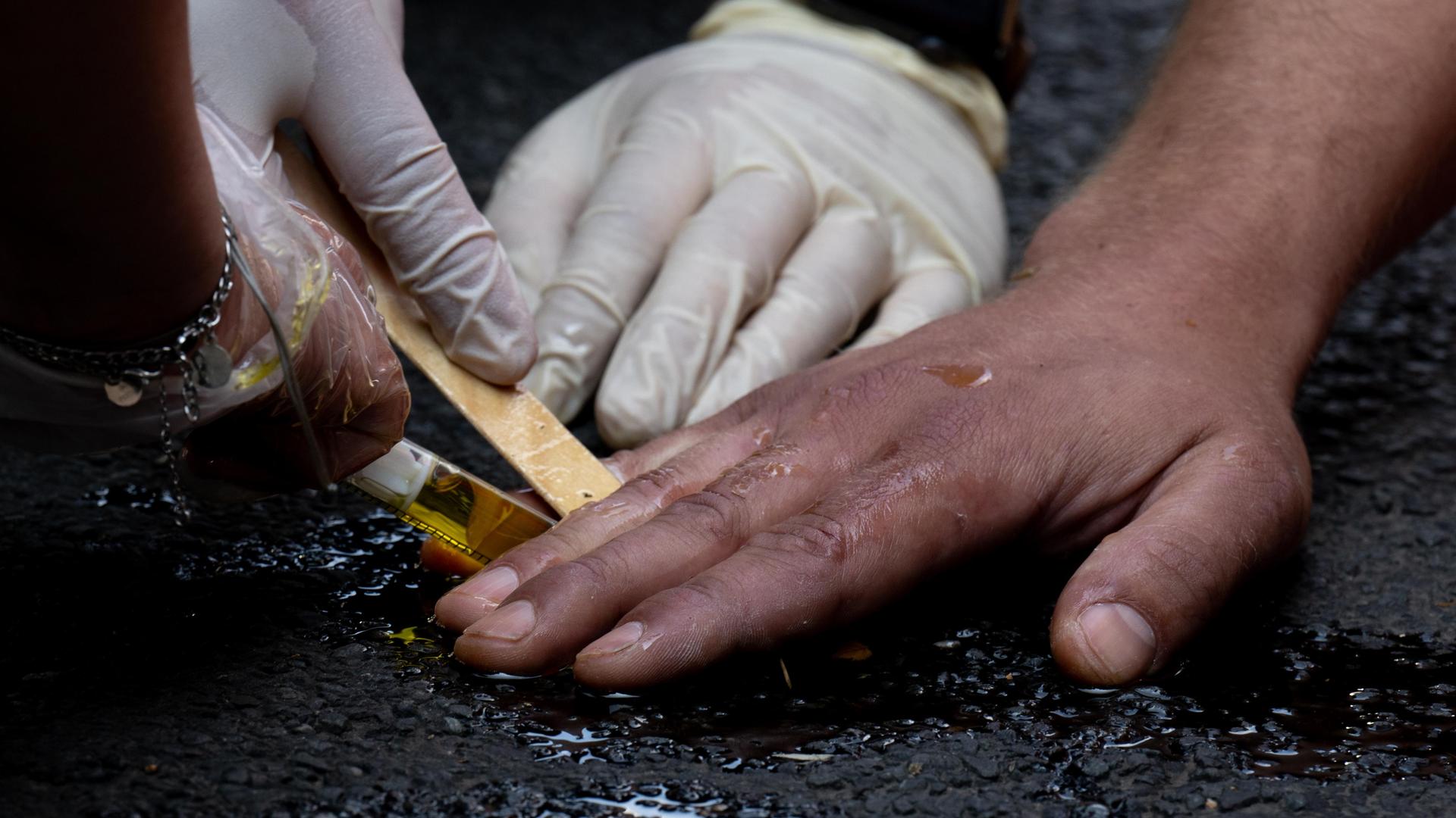 Polizeibeamte entfernen die festgeklebte Hand eines Klimaaktivisten der Gruppe "Letzte Generation" mit Olivenöl von einer Straße.