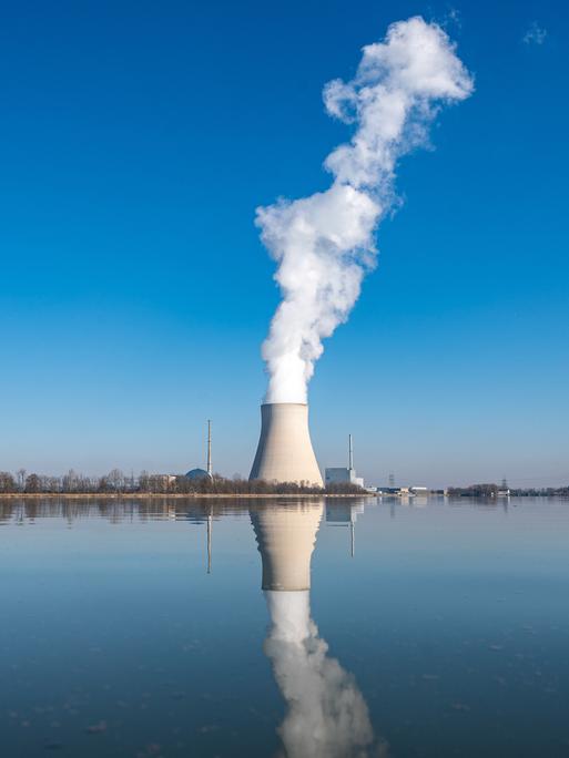 Aus dem Kühlturm eines Atomkraftwerks steigt weißer Dampf auf. Der Kühlturm spiegelt sich im Wasser. 