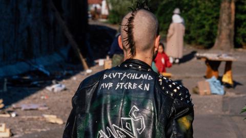 Ein Punker mit Nieten-Lederjacke mit den Aufschriften "Deutschland muß sterben", "No Future" und "Chaos" 