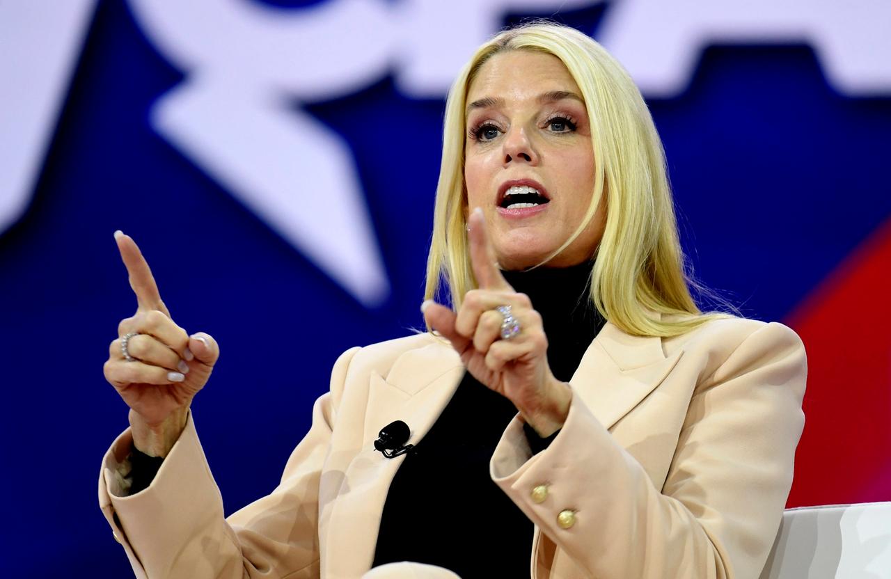 Pam Bondi, eine Frau mit langen blonden Haaren, einem schwarzen Rollkragenpulli und einem cremefarbenen Blazer spricht bei einem Kongress. Sie unterstützt ihre Aussage mit einer Geste in der beide Zeigefinger auf das Publikum gerichtet sind. 