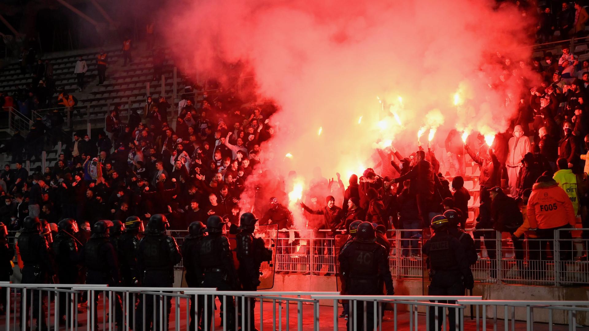 Hooligans beim Spiel Paris FC gegen Olympique Lyonnais im Jahr 2021. Sie feuern bengalisches Feuer ab, im Vordergrund stehen Polizisten. Hooligans beim Spiel Paris FC gegen Olympique Lyonnais im Jahr 2021. Sie feuern bengalisches Feuer ab, im Vordergrund stehen Polizisten.