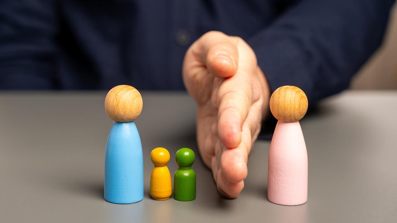 Eine Hand trennt eine blau angemalte Holzfigur zusammen mit zwei kleineren Holzfiguren von einer rosa Holzfigur.