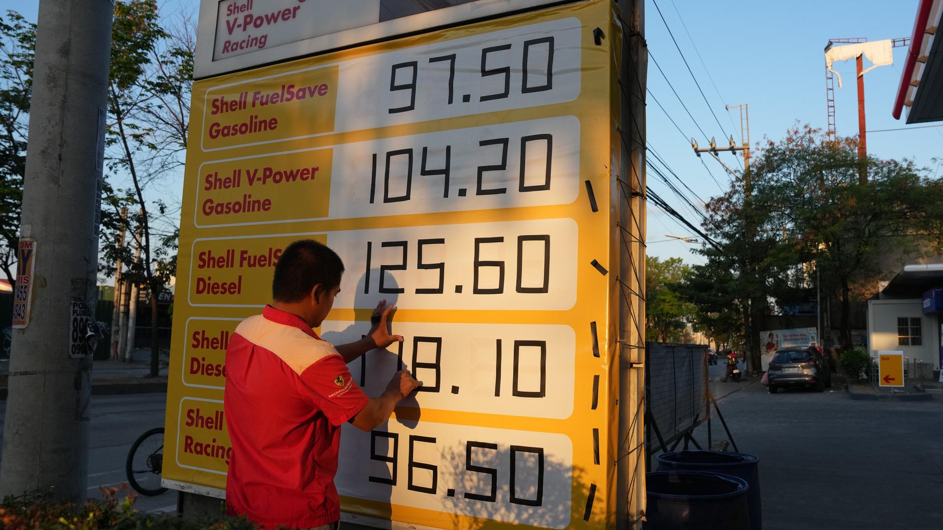 Philippinen: Ein Mann benutzt schwarzes Klebeband, um die Preise auf einem Schild an einer Tankstelle anzupassen. 