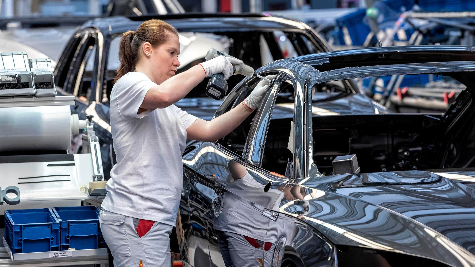 An der Montagelinie eines Autobauers steht eine Mitarbeiterin und bohrt eine Schraube an einem Automodell fest. 