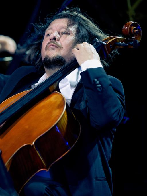 Im Vordergrund spielt Friedrich Kleinhapl mit einer wilden Geste auf seinem Violoncello. Im Hintergrund ist verschwommen Kima Barbier am Klavier zu erkennen.