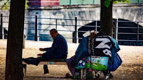 Ein Obdachloser sitzt auf einer Bank im Schatten der Bäume im Lustgarten auf der Museumsinsel in Berlin.