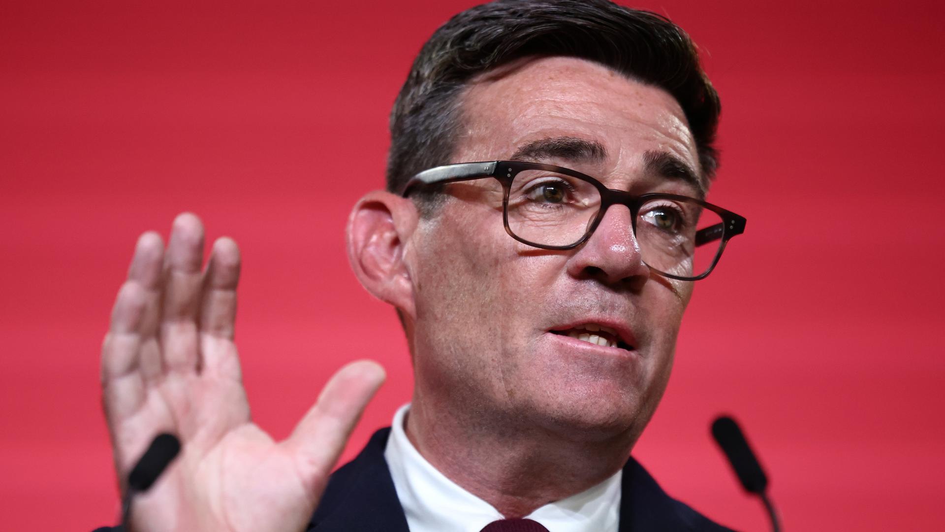 Andy Burnham spricht in ein Mikrofon und hebt die rechte Hand. Andy Burnham spricht in ein Mikrofon und hebt die rechte Hand.