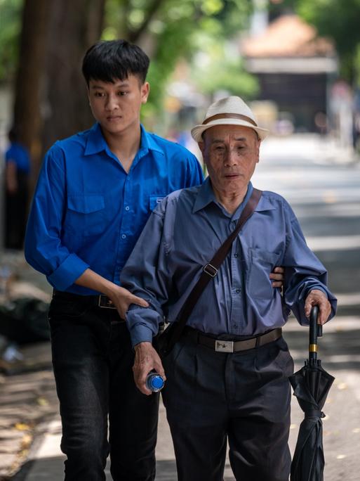 Ein junger Vietnamese hält einen älteren Mann am Arm und hilft ihm auf der Straße. (Symbolbild) Ein junger Vietnamese hält einen älteren Mann am Arm und hilft ihm auf der Straße. (Symbolbild)