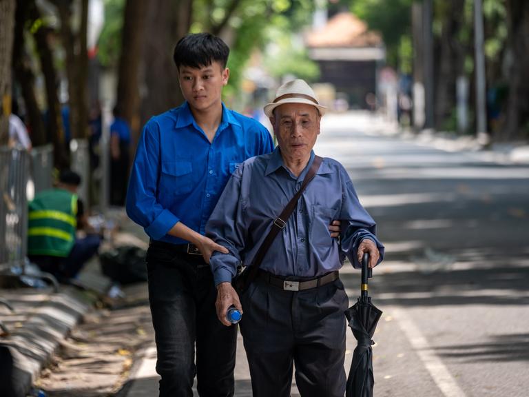 Ein junger Vietnamese hält einen älteren Mann am Arm und hilft ihm auf der Straße. (Symbolbild) Ein junger Vietnamese hält einen älteren Mann am Arm und hilft ihm auf der Straße. (Symbolbild)