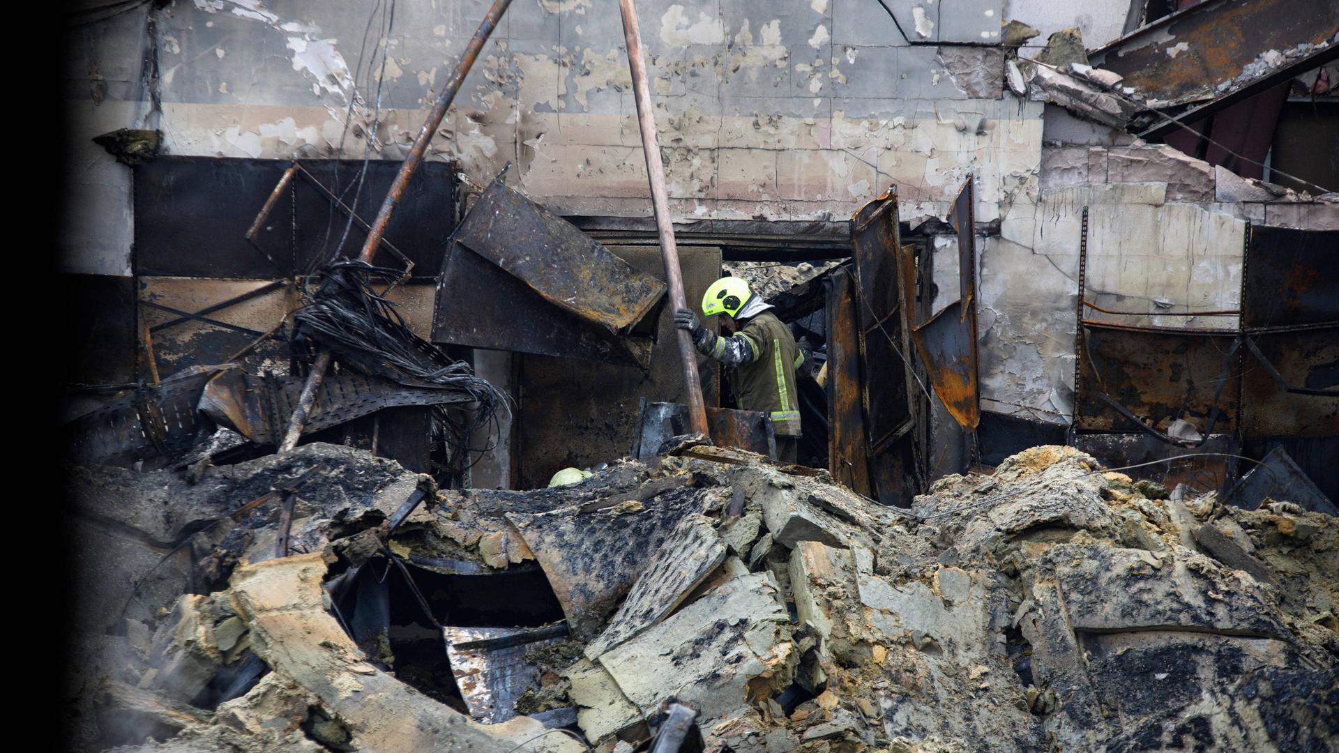 Ein Gebäude liegt nach einem Raketenangriff in Trümmern. In den Trümmern steht ein Feuerwehrmann, Ein Gebäude liegt nach einem Raketenangriff in Trümmern. In den Trümmern steht ein Feuerwehrmann,