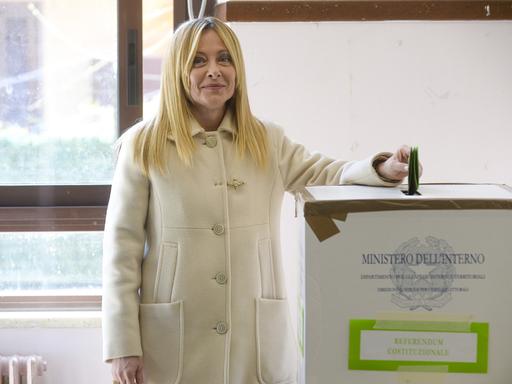 Italiens Ministerpräsidentin Meloni steckt ihren Wahlzettel in die Urne und lächelt dabei in die Kamera.