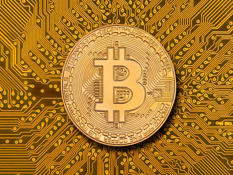 Eine Münze mit aufgeprägtem Bitcoin-Zeichen liegt über einem digitalen Netzwerk mit vielen Datenleitungen.