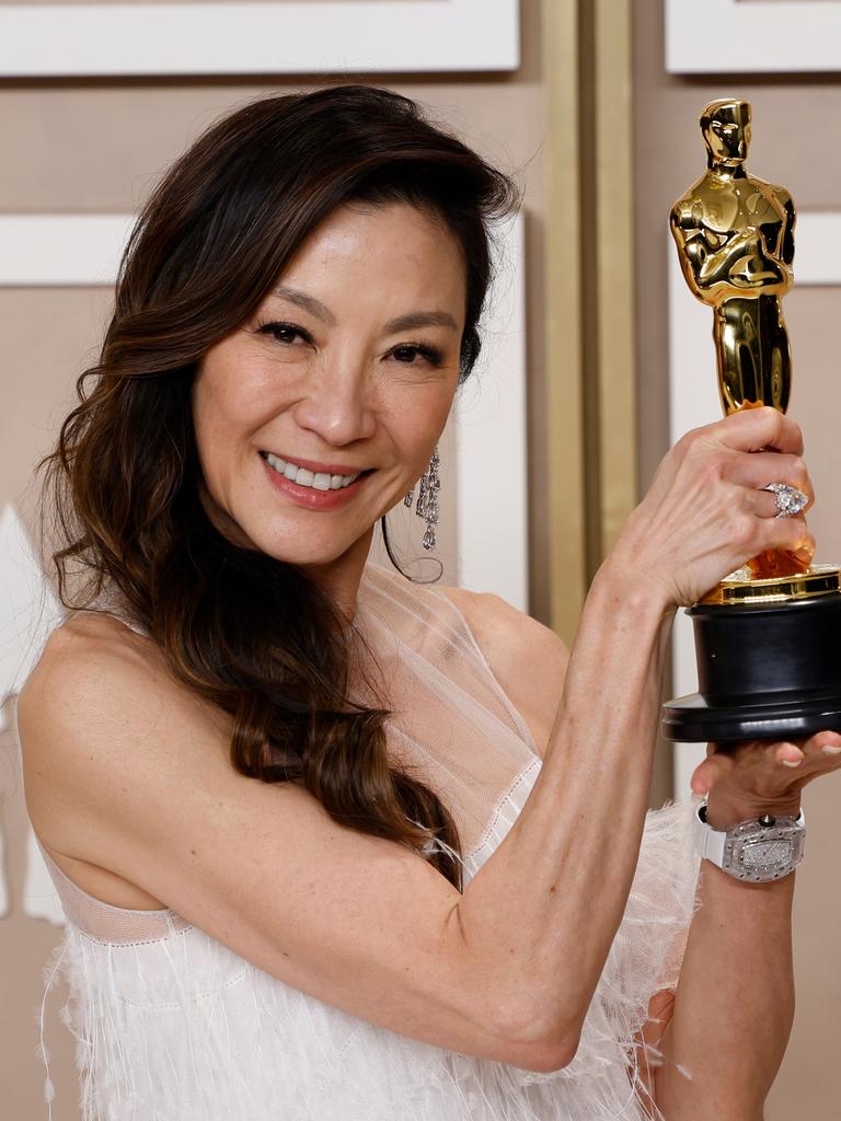 Die Schauspielerin Michelle Yeoh hält lächelnd ihre goldene Oscar-Statuette in die Kamera.