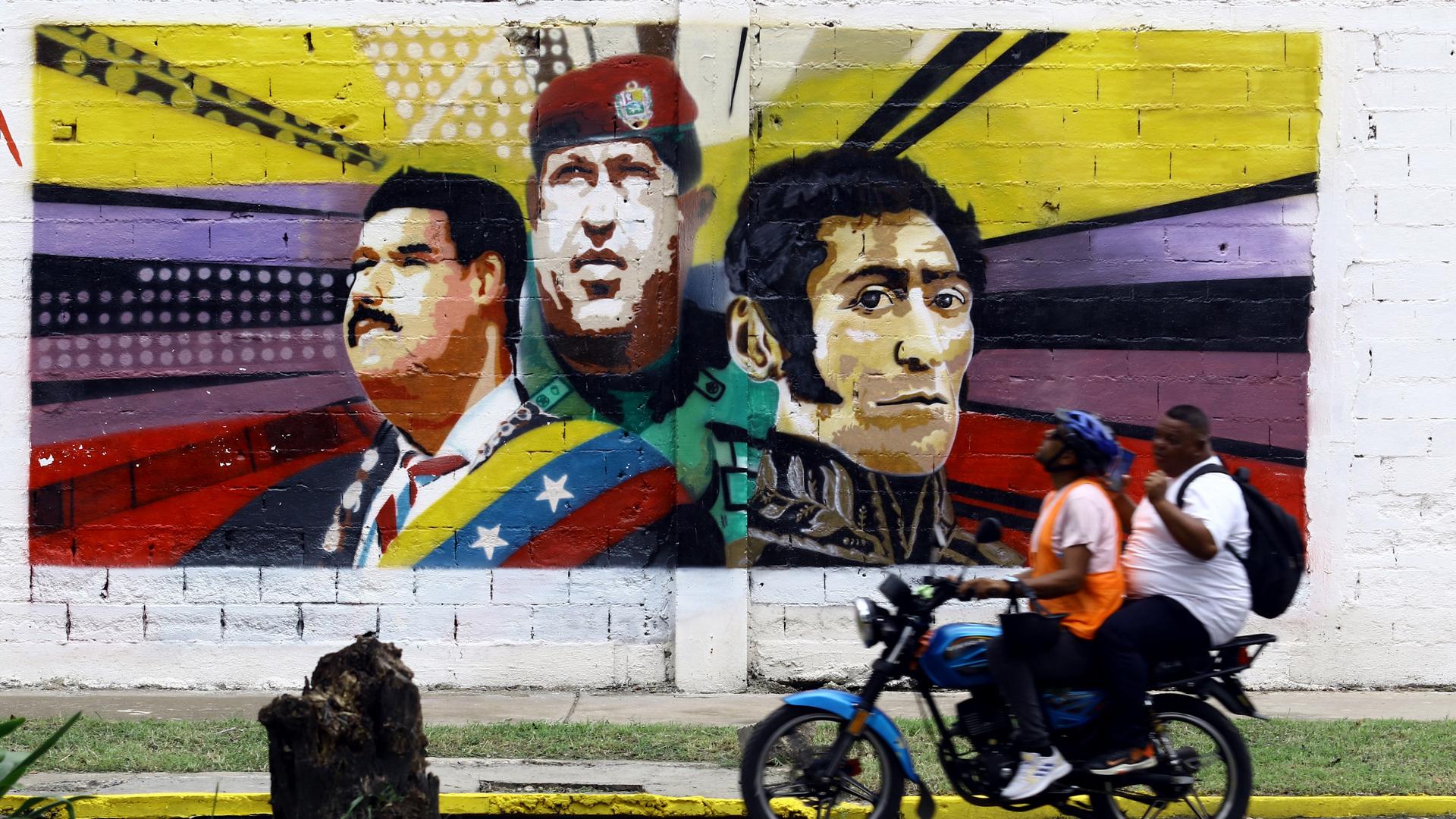 Ein Motorrad rollt an einem bunten Grafitto in Venezuela vorbei, auf dem unter anderem Hugo Chávez zu sehen ist.