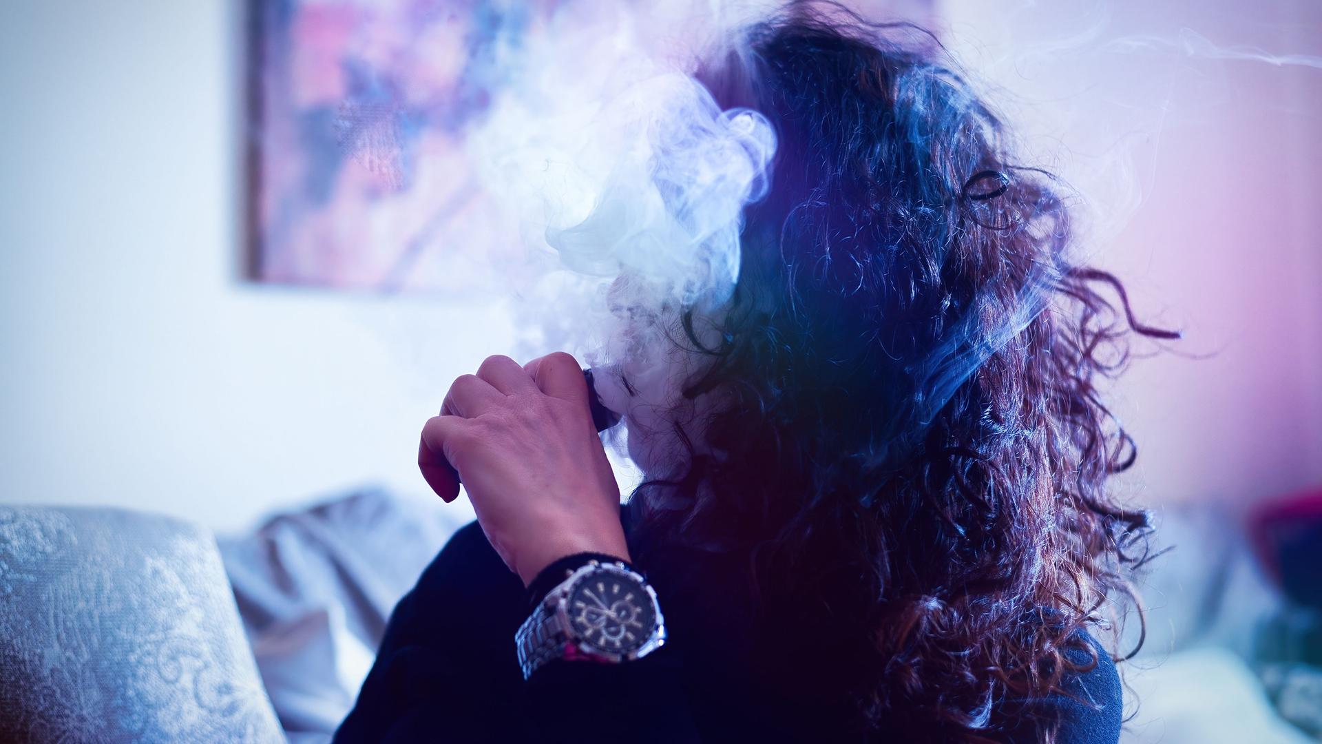 Eine junge Frau raucht eine E-Zigarette. Ihr Gesicht verschwindet hinter dem Dampf.