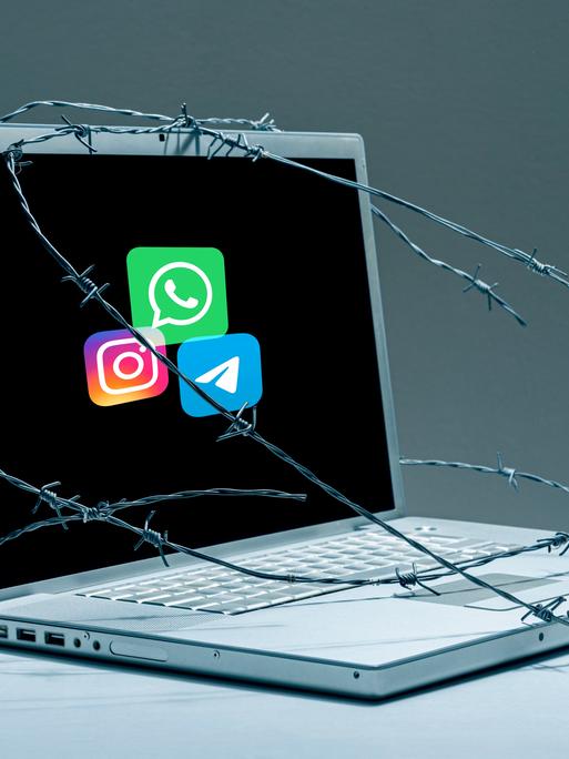 Auf einem mit Stacheldraht umwickelten Laptop sieht man die Logos von Telegram, Instagram und Whatsapp. 