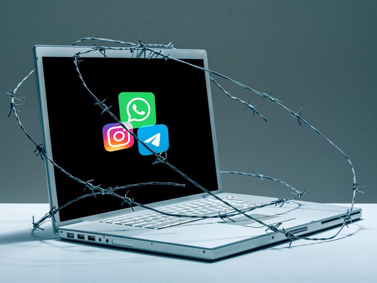 Auf einem mit Stacheldraht umwickelten Laptop sieht man die Logos von Telegram, Instagram und Whatsapp. 