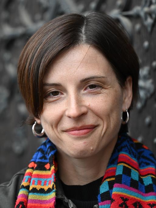 Dorothee Elmiger steht vor einer gusseisernen Tür, trägt einen bunten Schal und lächelt in die Kamera