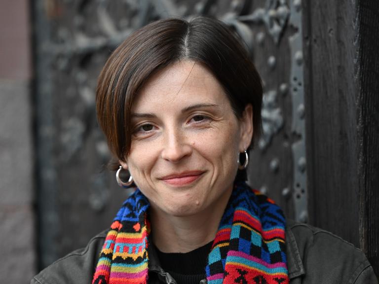 Dorothee Elmiger steht vor einer gusseisernen Tür, trägt einen bunten Schal und lächelt in die Kamera