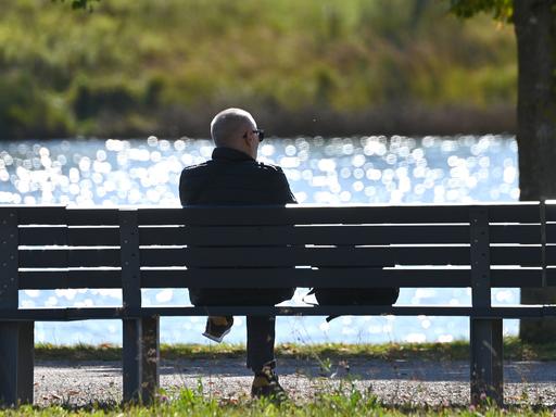Mann sitzt auf einer Bank im Freien