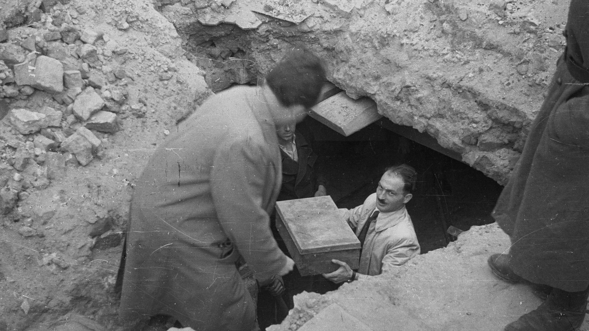Ein Helfer trägt eine Kiste mit Erinnerungen aus einem Erdlloch unter dem Warschauer Getto. Die Fundstücke bilden den Grundstock für das Ringelblum-Archiv. 