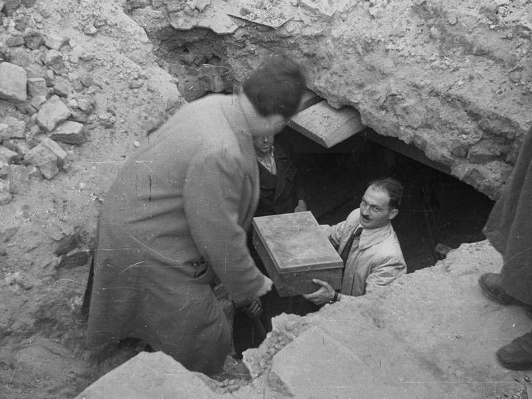 Ein Helfer trägt eine Kiste mit Erinnerungen aus einem Erdlloch unter dem Warschauer Getto. Die Fundstücke bilden den Grundstock für das Ringelblum-Archiv. 