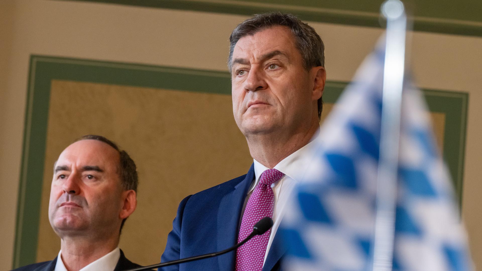 Hubert Aiwanger (li), Bundesvorsitzender der Freien Wähler, und Markus Söder (CSU), Ministerpräsident von Bayern. Beide tragen Krawatte, weißes Hemd und Sakko, rechts im Vordergrund etwas unscharf eine bayerische Landesfahne.