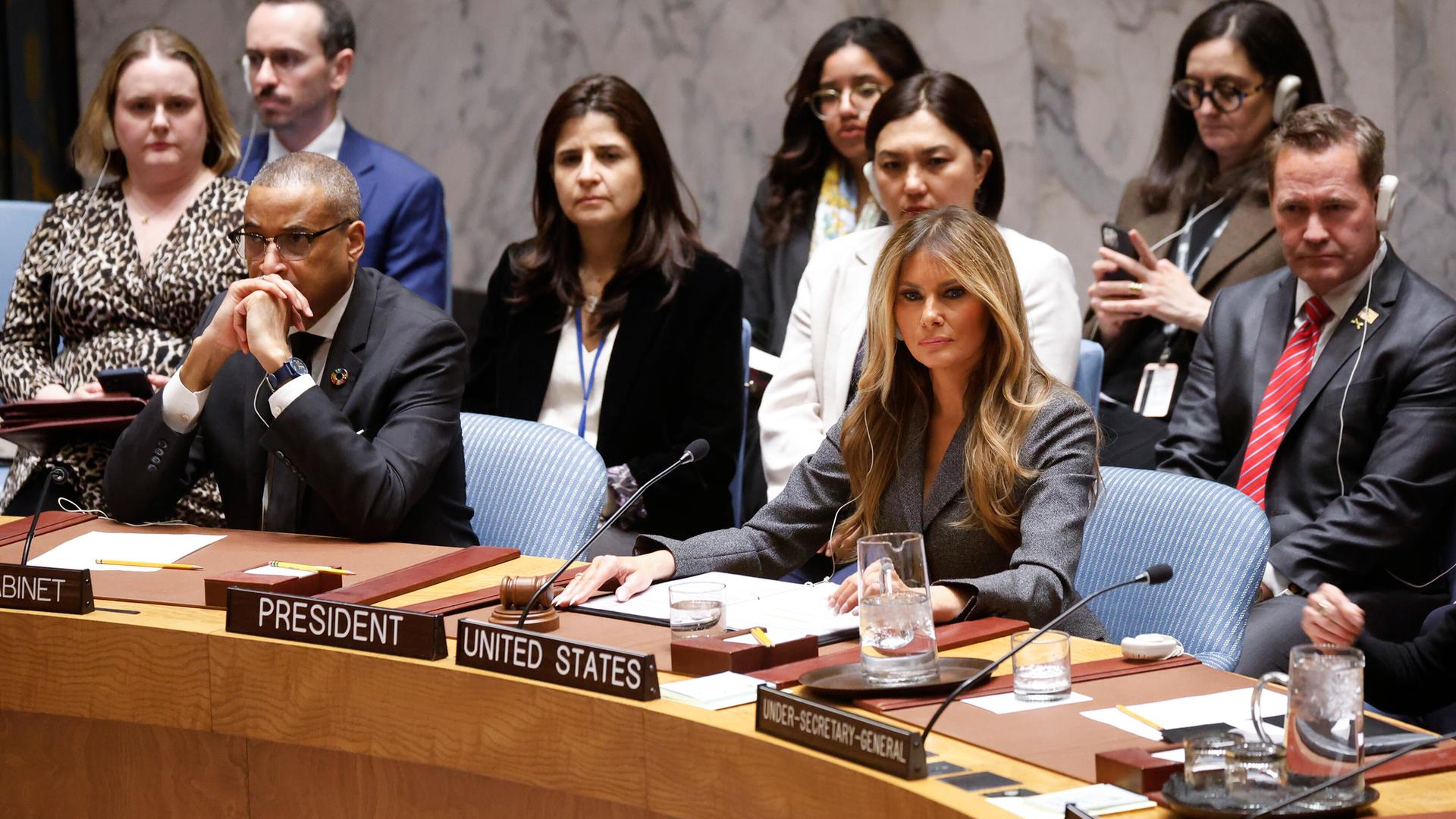 Das Bild zeigt die First Lady Melania Trump an einem braunen Holztisch umringt von verschiedenen UN-Mitarbeitern. Vor ihr ist ein Mikrophon aufgestellt. Das Bild zeigt die First Lady Melania Trump an einem braunen Holztisch umringt von verschiedenen UN-Mitarbeitern. Vor ihr ist ein Mikrophon aufgestellt.