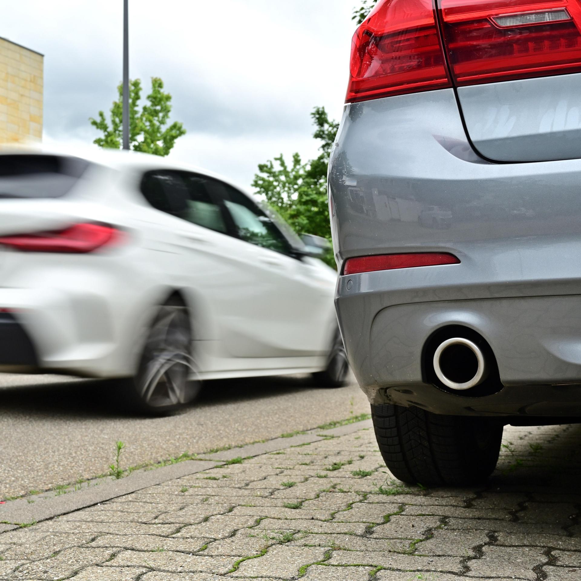 Ein Auto steht an einem Straßenrand. Groß um Bild ist der Auspuff zu sehen. 