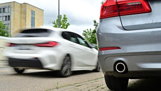 Ein Auto steht an einem Straßenrand. Groß um Bild ist der Auspuff zu sehen. 