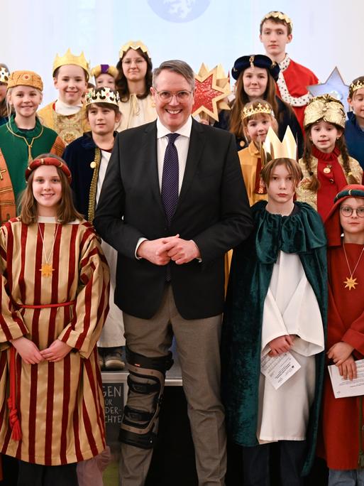 Alexander Schweitzer (M, SPD), Ministerpräsident von Rheinland-Pfalz, steht beim Empfang der Sternsinger im Festsaal der Staatskanzlei zwischen den Sternsingern des Bistums Mainz. 