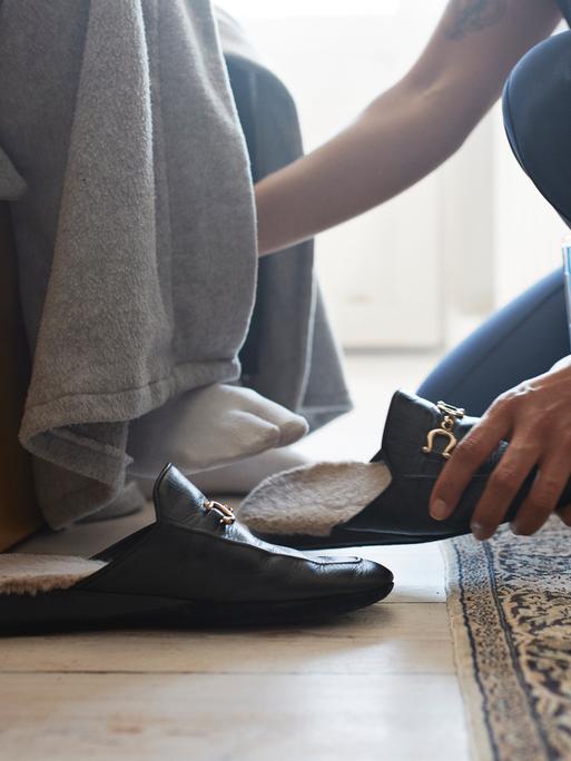 Eine jüngere Person hilft einer älteren Person beim Schuhe anziehen.