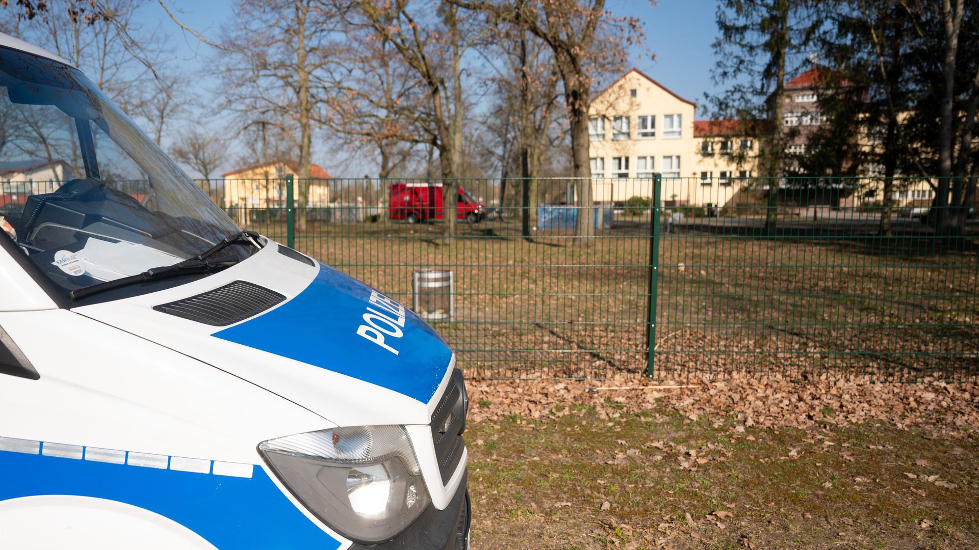 Ein Polizeiauto steht im Vordergrund des Bildes an einer Straße. Hinter einem Zaun befindet sich ein Schulgrundstück. Ein Polizeiauto steht im Vordergrund des Bildes an einer Straße. Hinter einem Zaun befindet sich ein Schulgrundstück.