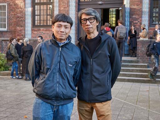 Die Ruangrupa-Mitglieder Reza Afisina (l) und Iswanto Hartono stehen vor dem Eingang der Hochschule für bildende Künste Hamburg