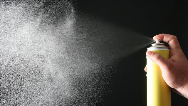 Eine Hand hält eine gelbfarbene Spraydose und sprayt. Der Sprühnebel ist gut erkennbar.