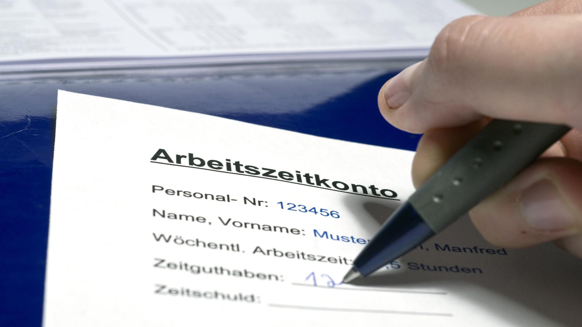 Jemand schreibt mit einem Kugelschreiber seine Überstunden auf einem Arbeitszeitkonto-Formular auf. Jemand schreibt mit einem Kugelschreiber seine Überstunden auf einem Arbeitszeitkonto-Formular auf.