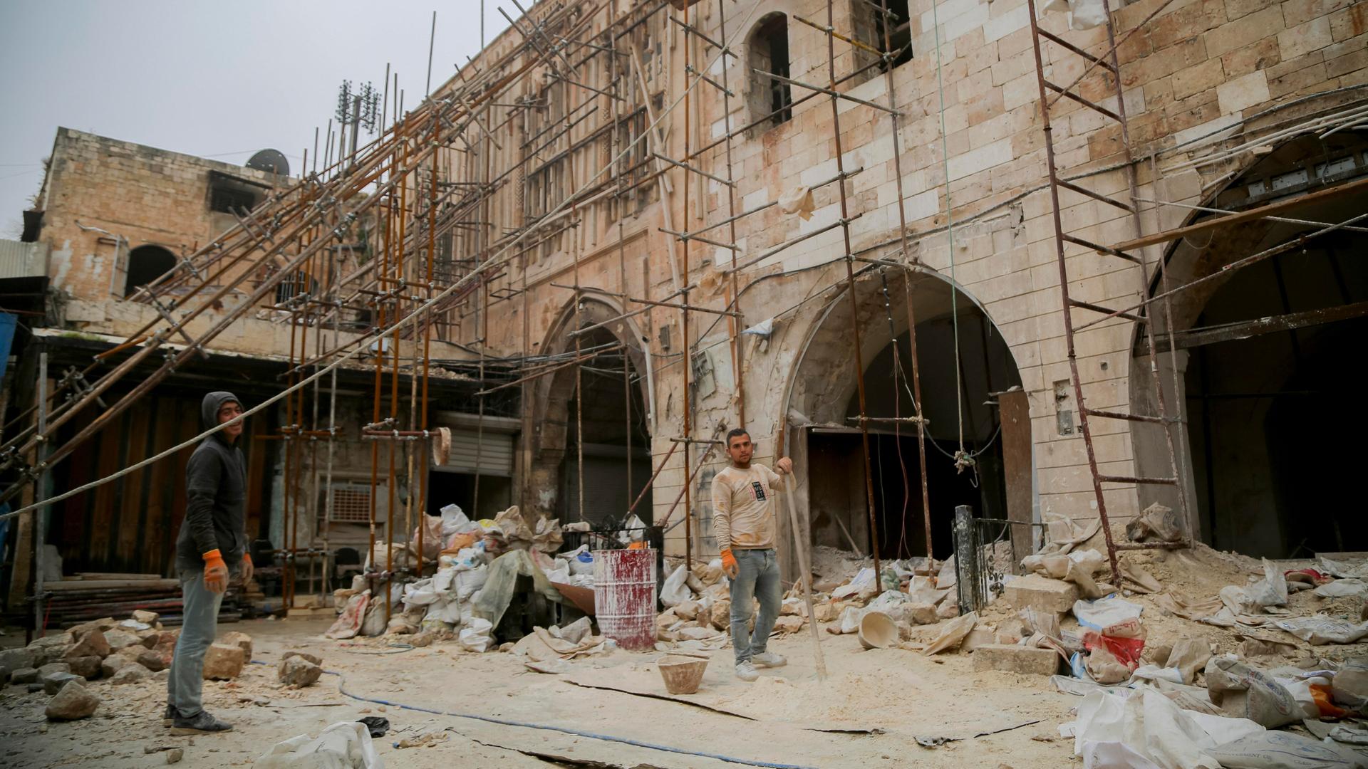 An einem zerstörten Gebäude in Aleppo steht ein Gerüst, davor Arbeiter beim Aufbau