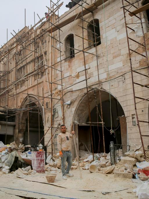 An einem zerstörten Gebäude in Aleppo steht ein Gerüst, davor Arbeiter beim Aufbau