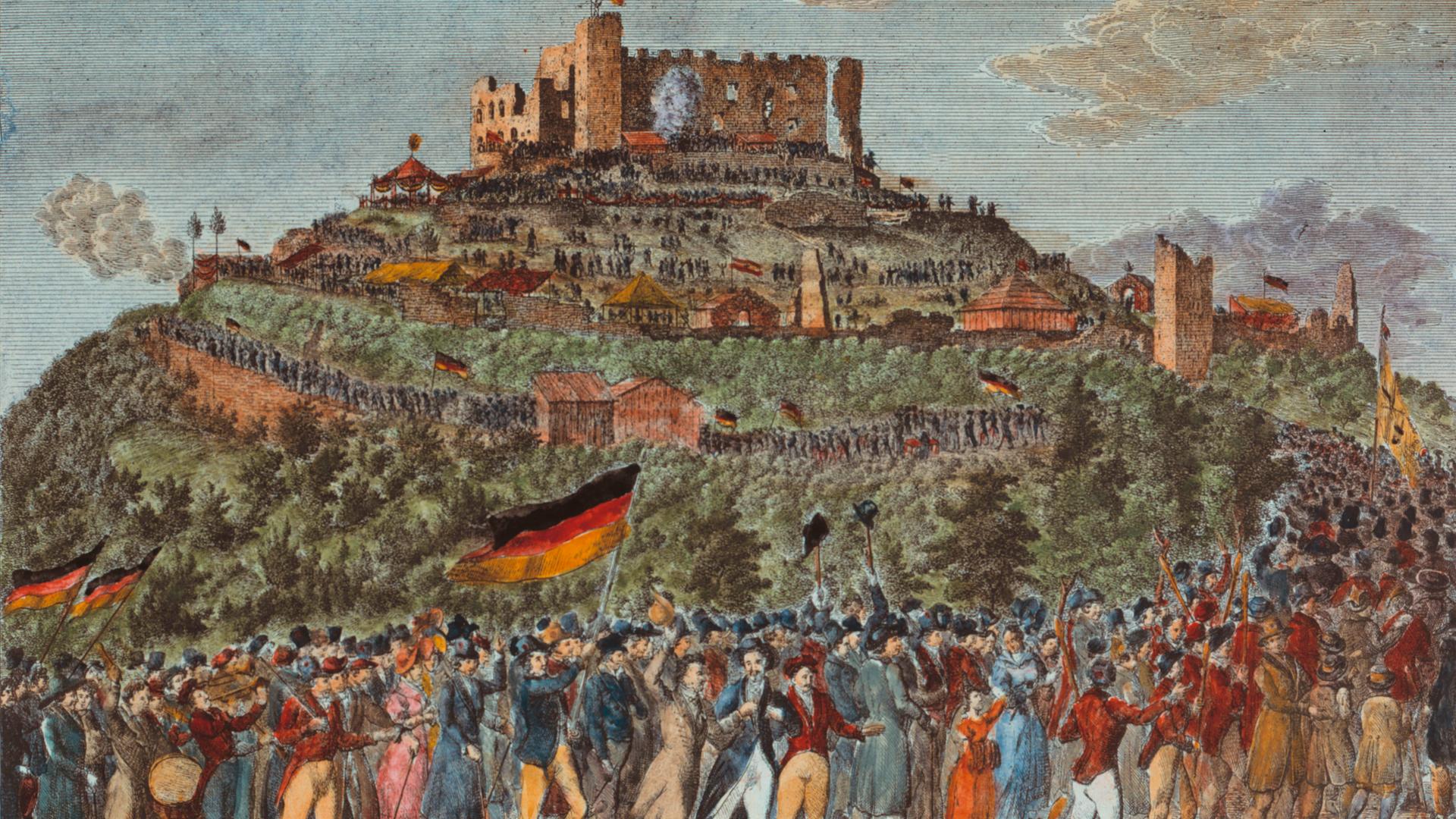 Das Bild aus dem Jahr 1832 zeigt eine Panorama-Perspektive auf das Schloss Hambach mit einem langen Menschenzug, der darauf zuhält. Die Leute schwenken Fahnen in den Farben Schwarz-Rot-Gold.