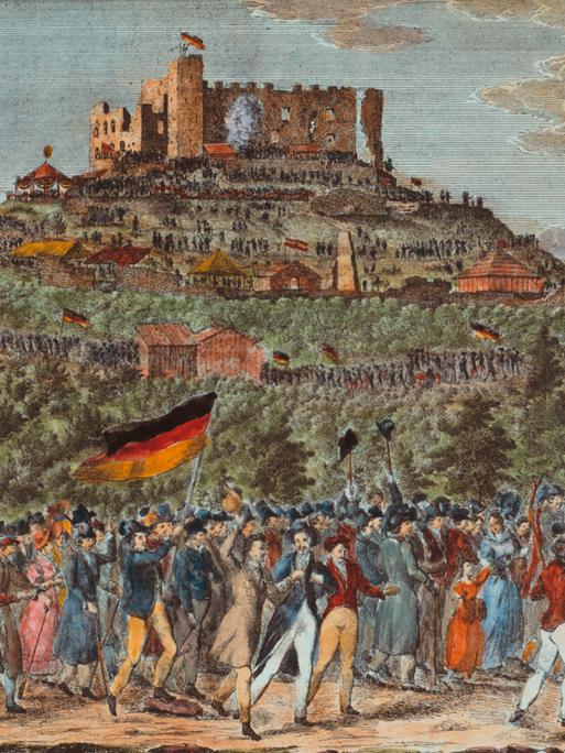 Das Bild aus dem Jahr 1832 zeigt eine Panorama-Perspektive auf das Schloss Hambach mit einem langen Menschenzug, der darauf zuhält. Die Leute schwenken Fahnen in den Farben Schwarz-Rot-Gold.