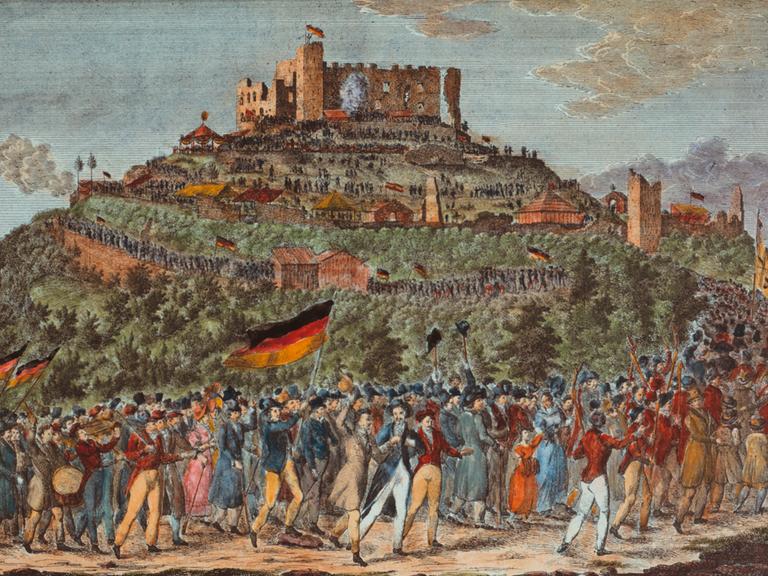 Das Bild aus dem Jahr 1832 zeigt eine Panorama-Perspektive auf das Schloss Hambach mit einem langen Menschenzug, der darauf zuhält. Die Leute schwenken Fahnen in den Farben Schwarz-Rot-Gold.