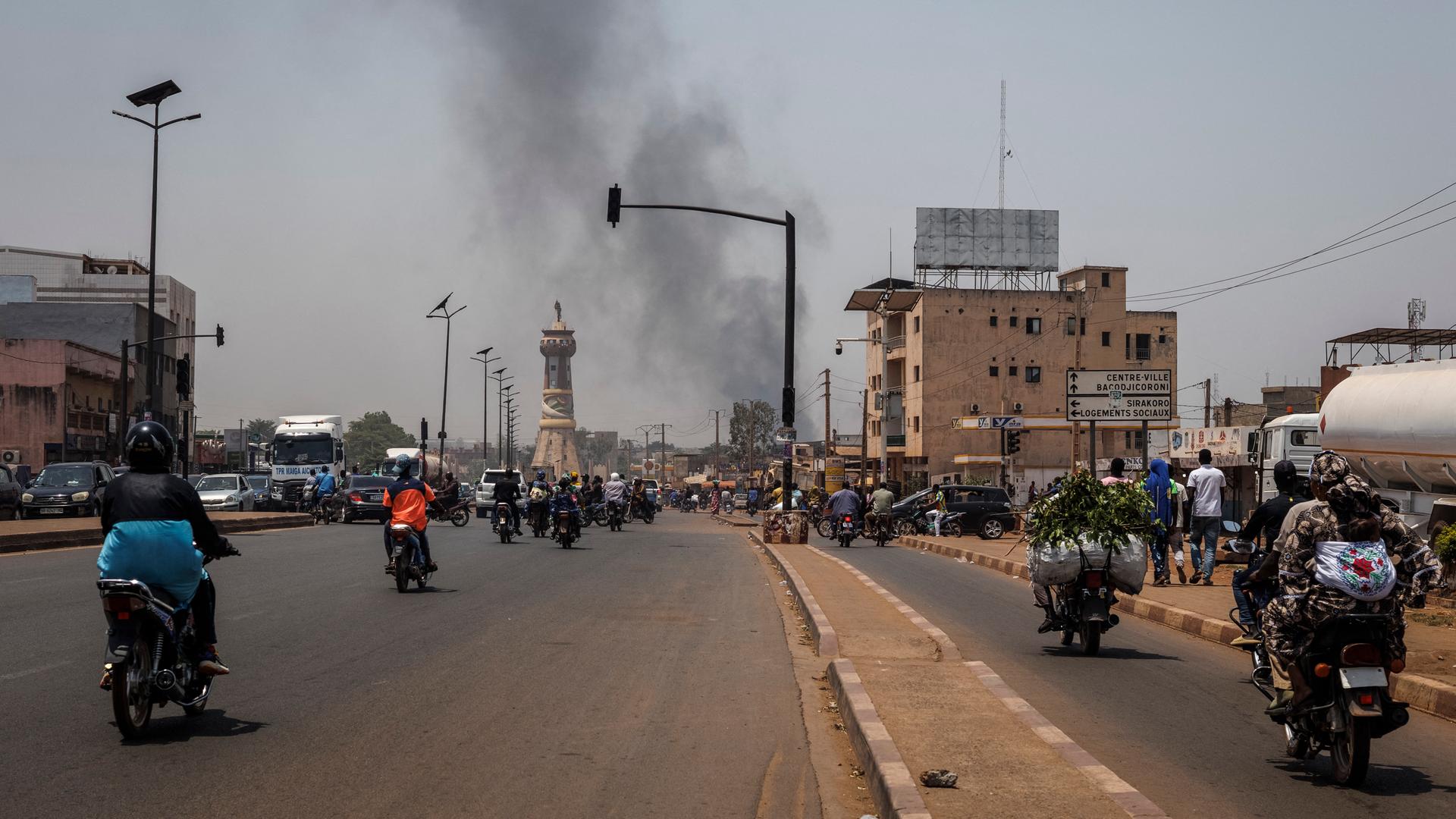 Eine schwarze Rauchsäule steigt über den Gebäuden auf, während der Verkehr am Africa Tower-Denkmal in Bamako vorbeifährt.