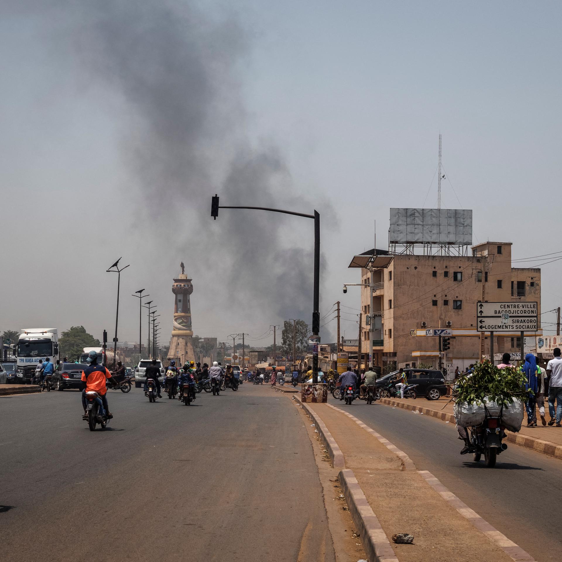 Eine schwarze Rauchsäule steigt über den Gebäuden auf, während der Verkehr am Africa Tower-Denkmal in Bamako vorbeifährt.