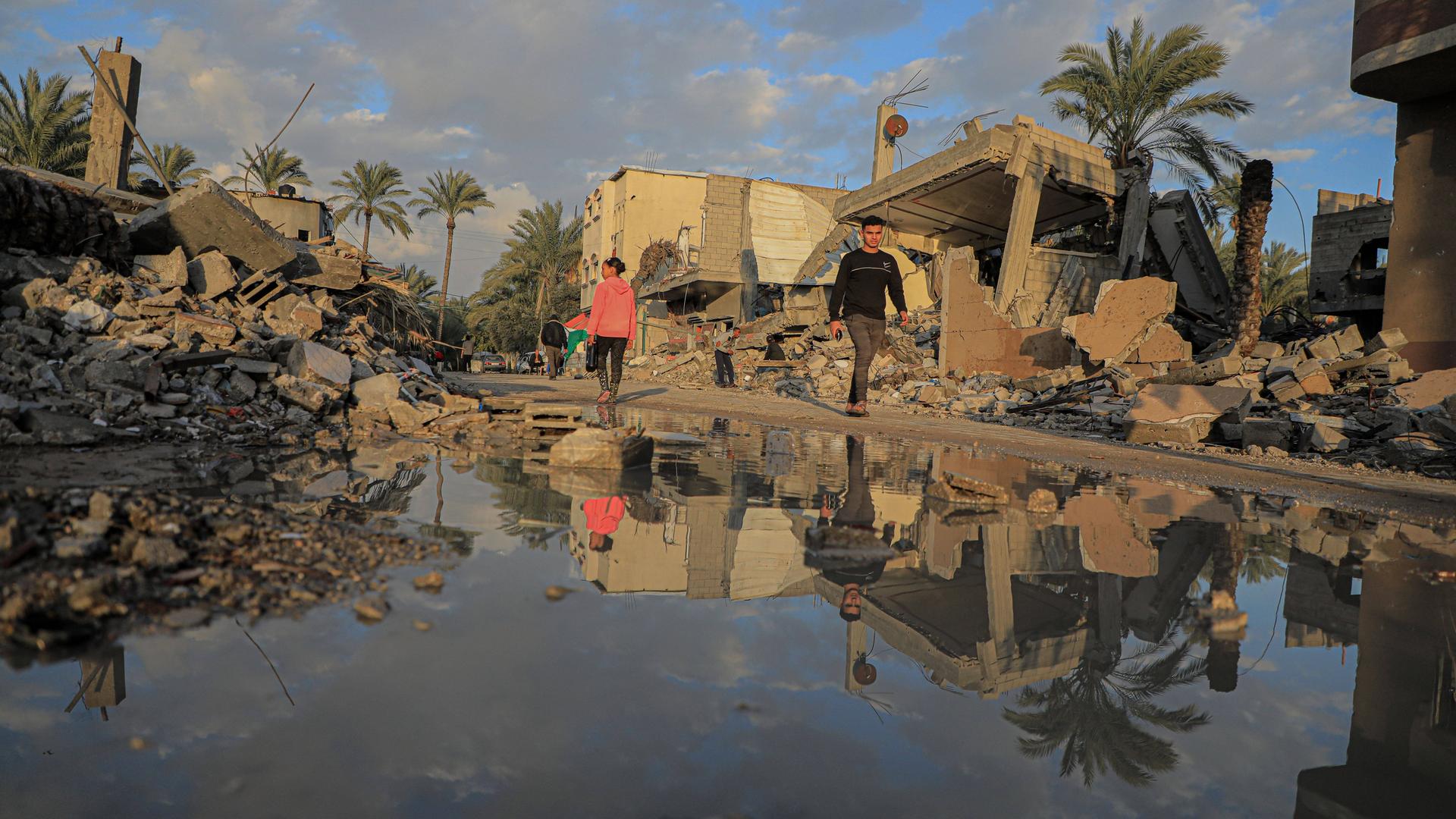 Menschen gehen am 14. Januar 2024 an zerstörten Gebäuden in der Stadt Deir el-Balah im Zentrum des Gazastreifens vorbei.
