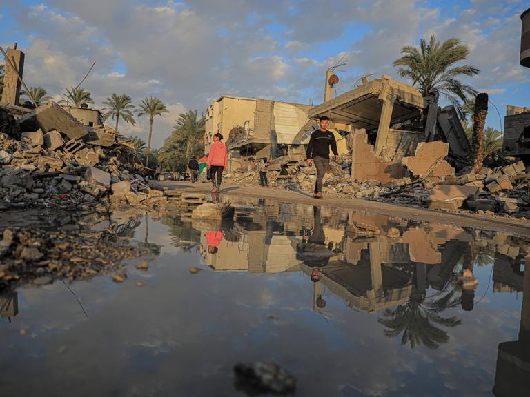 Menschen gehen am 14. Januar 2024 an zerstörten Gebäuden in der Stadt Deir el-Balah im Zentrum des Gazastreifens vorbei.